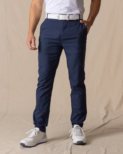 Men's Maverick Twill Pant in New Indigo, front view on model featuring solid navy slim fit golf pants with white belt and white shoes