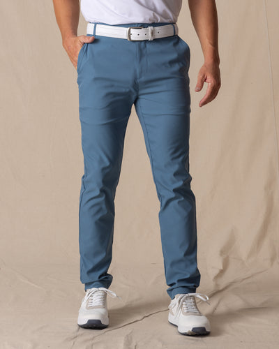 Men's Maverick Twill Pant in Petrol, front view on model featuring solid petrol blue slim fit golf pants with white belt and white golf shoes