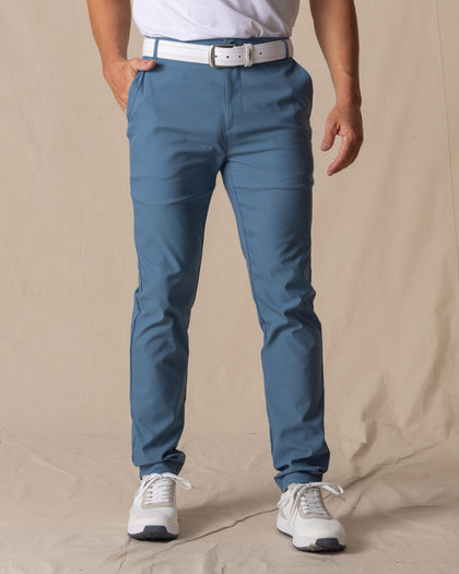 Men's Maverick Twill Pant in Petrol, front view on model featuring solid petrol blue slim fit golf pants with white belt and white golf shoes
