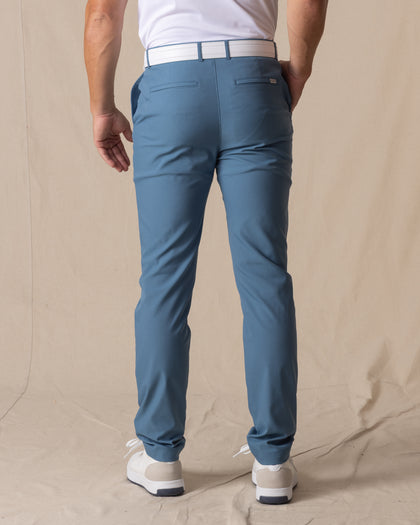 Men's Maverick Twill Pant in Petrol, back view on model featuring solid petrol blue golf pants with white belt and white golf shoes