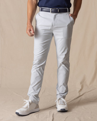 Men's Maverick Twill Pant in Silver, front view on model featuring solid silver slim fit golf pants with navy belt and white golf shoes