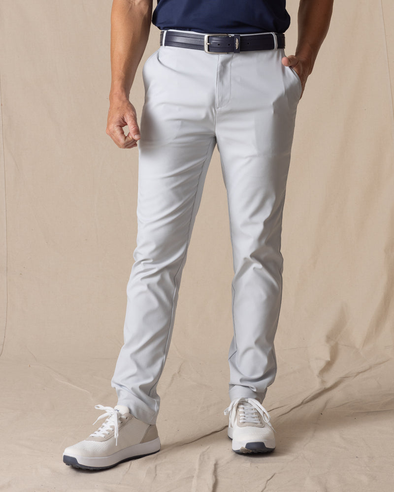 Men's Maverick Twill Pant in Silver, front view on model featuring solid silver slim fit golf pants with navy belt and white golf shoes