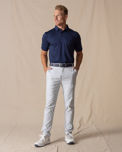 Men's Maverick Twill Pant in Silver, full length front view on model featuring solid silver slim fit golf pants paired with a navy polo, navy belt, and white golf shoes