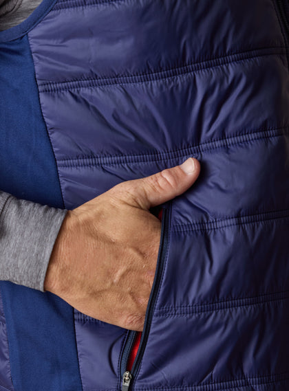 Men's Delta Vest in Indigo, close-up side detail featuring zip hand pocket, horizontal quilted baffles, and contrast softshell side panel with red interior lining