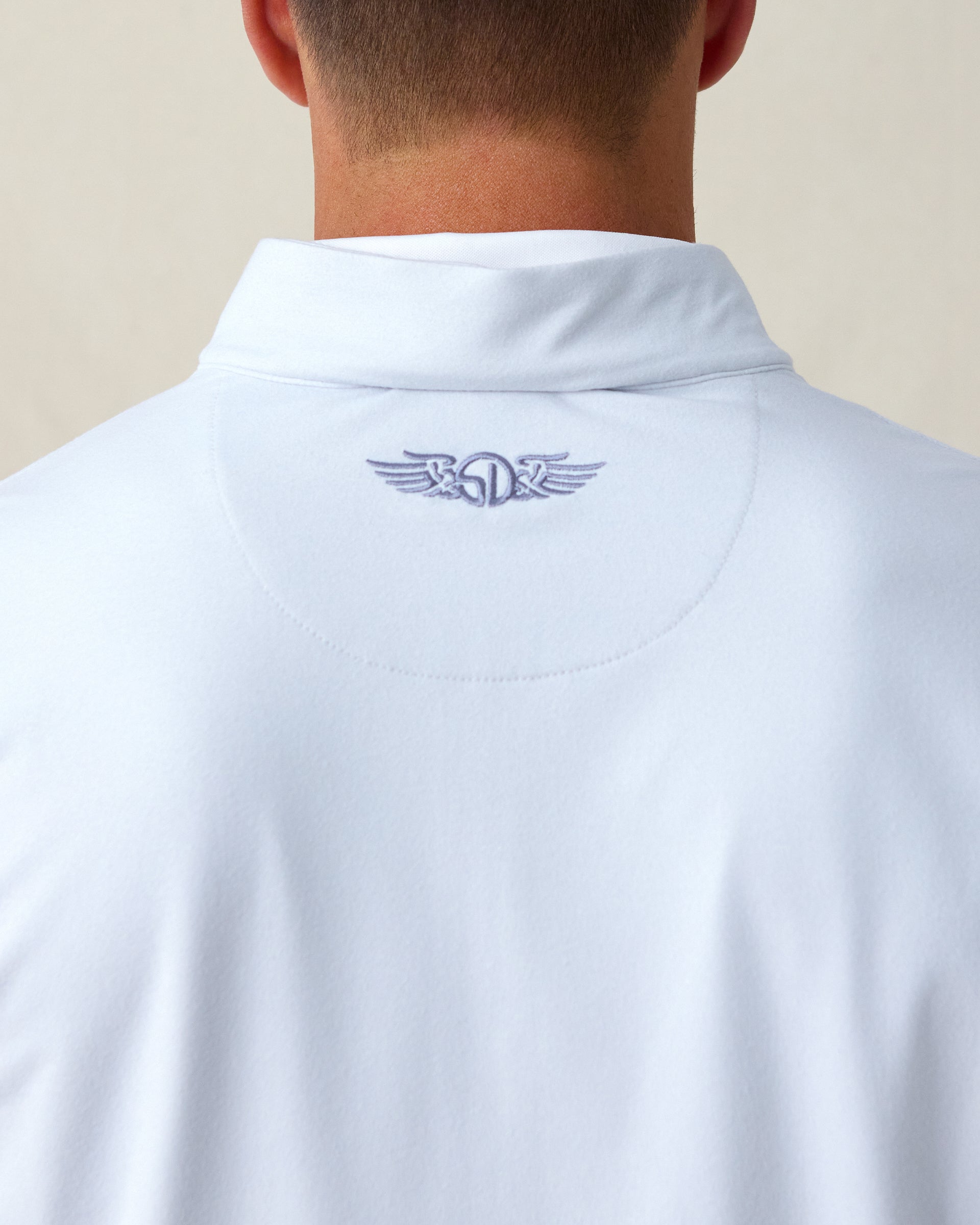 Close-up of the embroidered logo detail just below the collar on the back of the Ballard Quarter Zip in silver