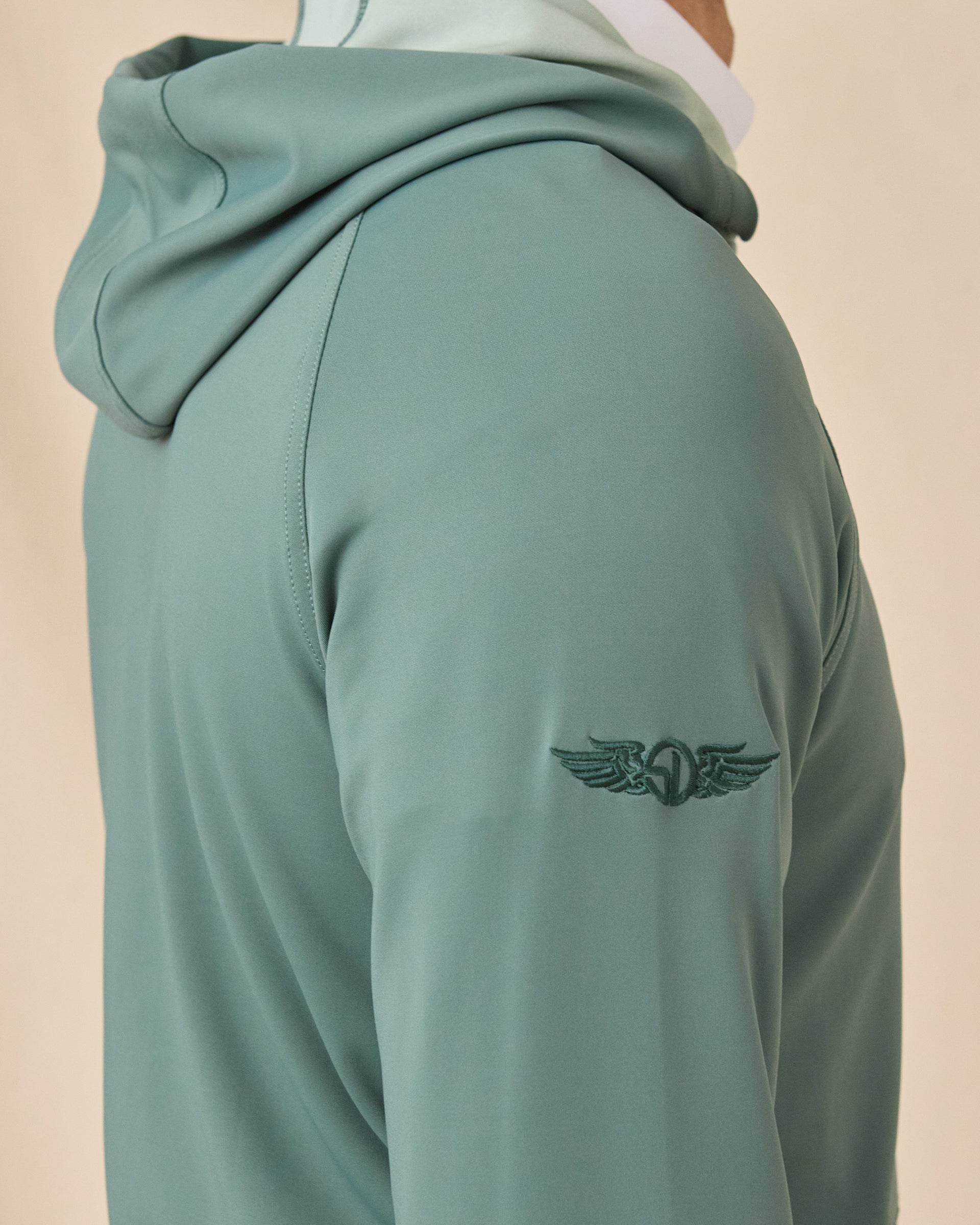 Close-up of the Mackenzie Hoodie in Dark Forest showing the hood, raglan shoulder seam, and tonal embroidered logo on the sleeve.