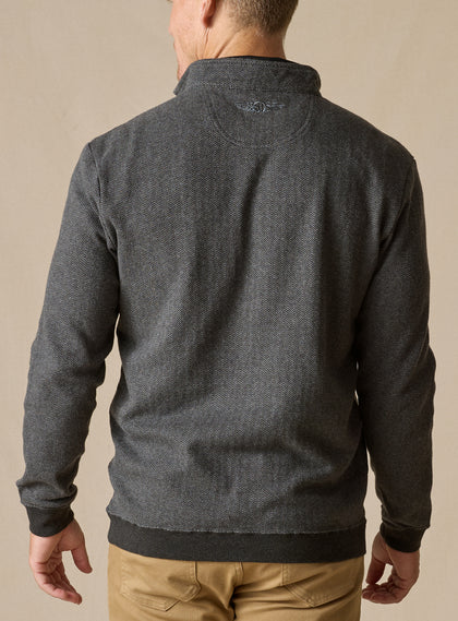 Men's Harrison Quarter Zip in Black, back model view featuring a charcoal herringbone knit body with tonal logo embroidery at the upper back, layered over a black collared shirt with khaki pants