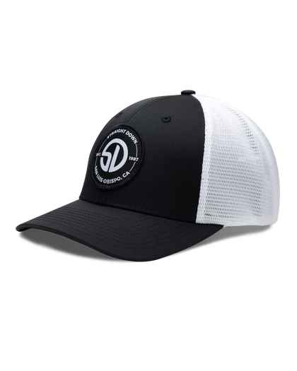 Circle Hat in Black White, side view featuring a black structured trucker cap with a circular embroidered patch featuring the SD monogram logo encircled by "Straight Down Est. 1987 San Luis Obispo, CA" text on the front panel, with white mesh back panels