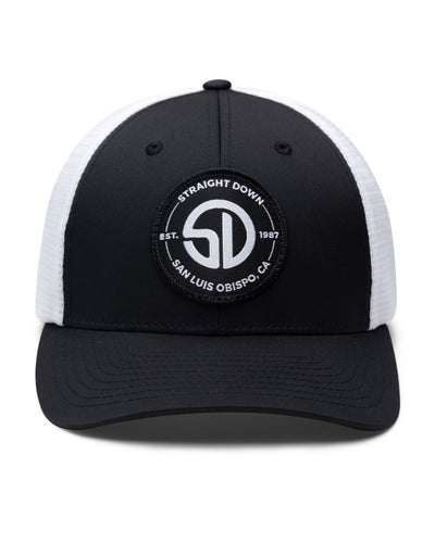 Circle Hat in Black White, front view featuring a black structured trucker cap with a circular embroidered patch featuring the SD monogram logo encircled by "Straight Down Est. 1987 San Luis Obispo, CA" text on the front panel, with white mesh back panels