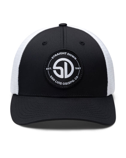 Circle Hat in Black White, front view featuring a black structured trucker cap with a circular embroidered patch featuring the SD monogram logo encircled by "Straight Down Est. 1987 San Luis Obispo, CA" text on the front panel, with white mesh back panels
