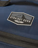 Straight Down Montana Cooler Bag in New Indigo, close-up detail view highlighting the rubber Straight Down mountain badge logo patch on the navy ripstop nylon exterior above the zip closure