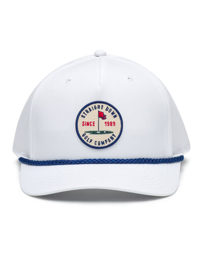 Pin High Rope Hat in White, front view featuring a Straight Down Golf Company circular patch depicting a golf hole with a red flag and "Since 1989" text, on a white hat with a blue rope brim detail