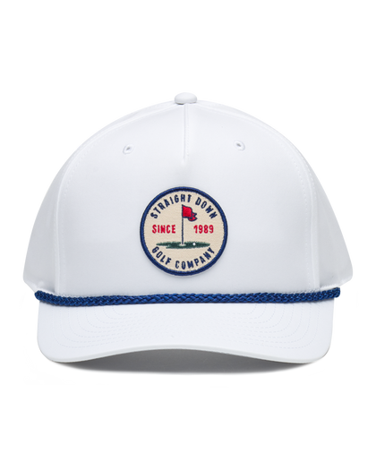 Pin High Rope Hat in White, front view featuring a Straight Down Golf Company circular patch depicting a golf hole with a red flag and "Since 1989" text, on a white hat with a blue rope brim detail