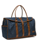 Angled view of the navy waxed canvas duffle bag, showcasing its structured shape, brown leather detailing, brass buckle closure, and exterior side pocket.