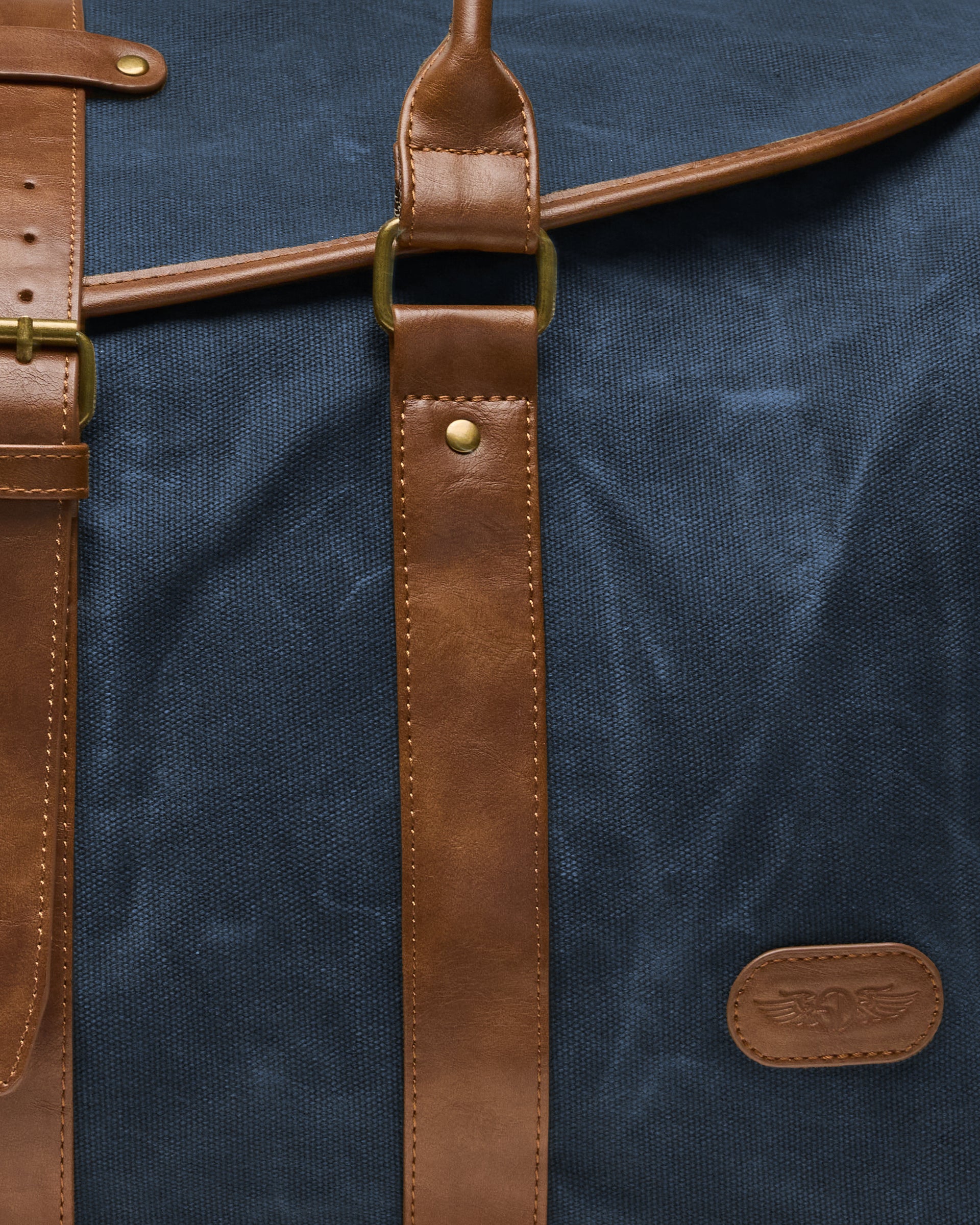 Close-up of the Waxed Canvas Duffle Bag in Navy, highlighting the textured canvas, stitched brown leather straps, brass hardware, and embossed Straight Down winged logo patch.