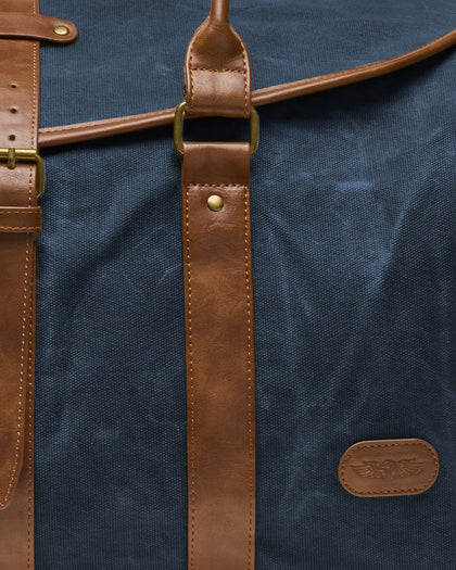 Close-up of the Waxed Canvas Duffle Bag in Navy, highlighting the textured canvas, stitched brown leather straps, brass hardware, and embossed Straight Down winged logo patch.