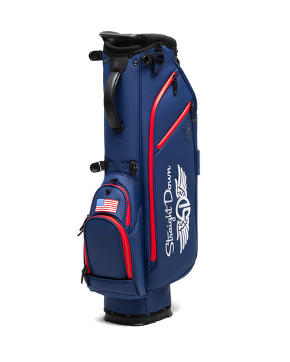 Straight Down Lux Carry Stand Bag in Navy Red, three-quarter front view featuring white Straight Down wing logo, red zipper accents, American flag patch on lower front pocket, and black top handle