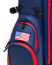 Straight Down Lux Carry Stand Bag in Navy Red, close-up detail view of lower front pocket section featuring embroidered American flag patch, red zipper trim, black zipper pulls, and navy blue structured pockets