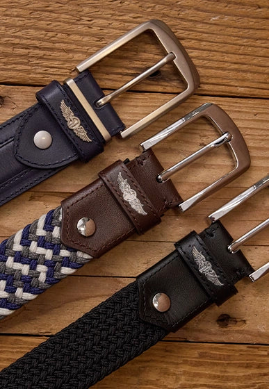 Close-up of three men’s belts in braided and leather styles with metal buckles, displayed on a wooden surface
