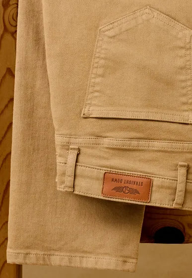 Close-up of tan denim pants showing a back pocket, belt loops, and a brown leather patch with the brand name 'Straight Down' printed on it.
