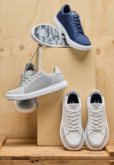Men’s golf sneakers in navy, gray, and white displayed on wooden blocks, showing both top and sole views.
