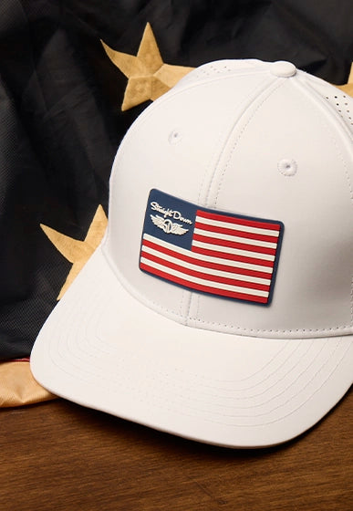 Close-up of white golf cap with American flag patch and Straight Down logo, set against a flag backdrop