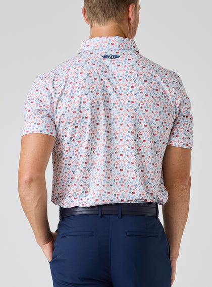 Grillin' Polo in White, on model back view showing the all-over scattered Fourth of July themed print in red and blue tones on a white base with Straight Down logo at the upper back, styled with navy pants and a navy belt