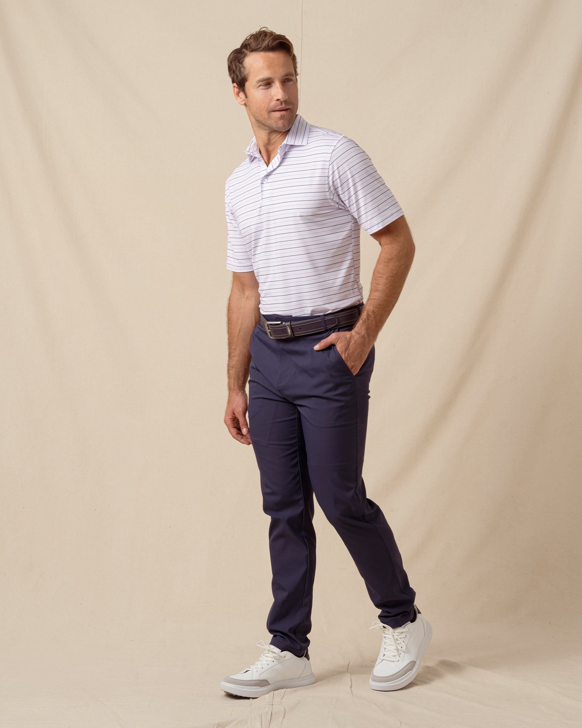 Men’s lilac striped polo styled with navy pants, brown belt, and white sneakers