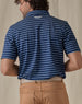Men's Quintero Stripe Polo in Green Stone, back view on model featuring a navy base with light blue horizontal stripe pattern with a Straight Down logo embroidered at the upper back, paired with tan pants