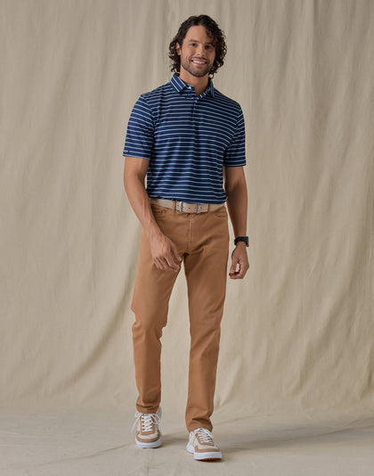Men's Quintero Stripe Polo in Green Stone, full-length front view on model featuring a navy base with light blue horizontal stripe pattern, paired with tan pants, a tan leather belt, and tan and white shoes