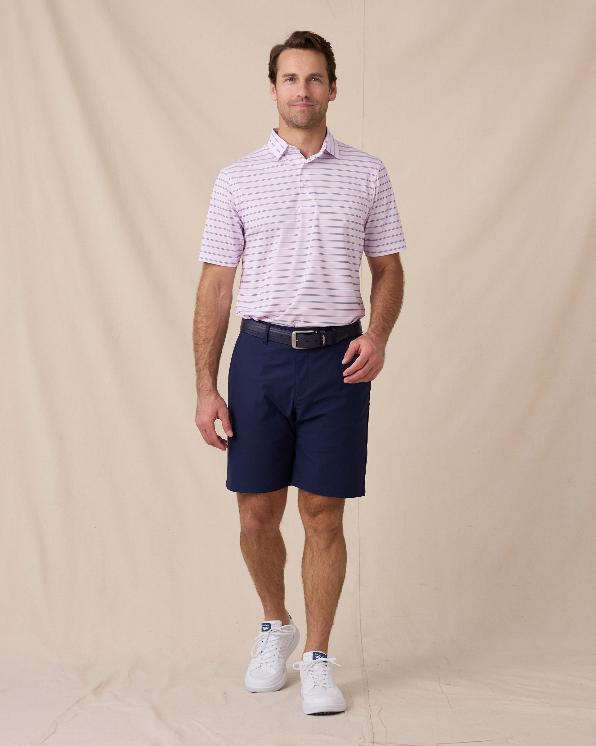 Model wearing the Quintero Stripe Polo in Lilac paired with navy golf shorts, a navy belt, and white golf shoes