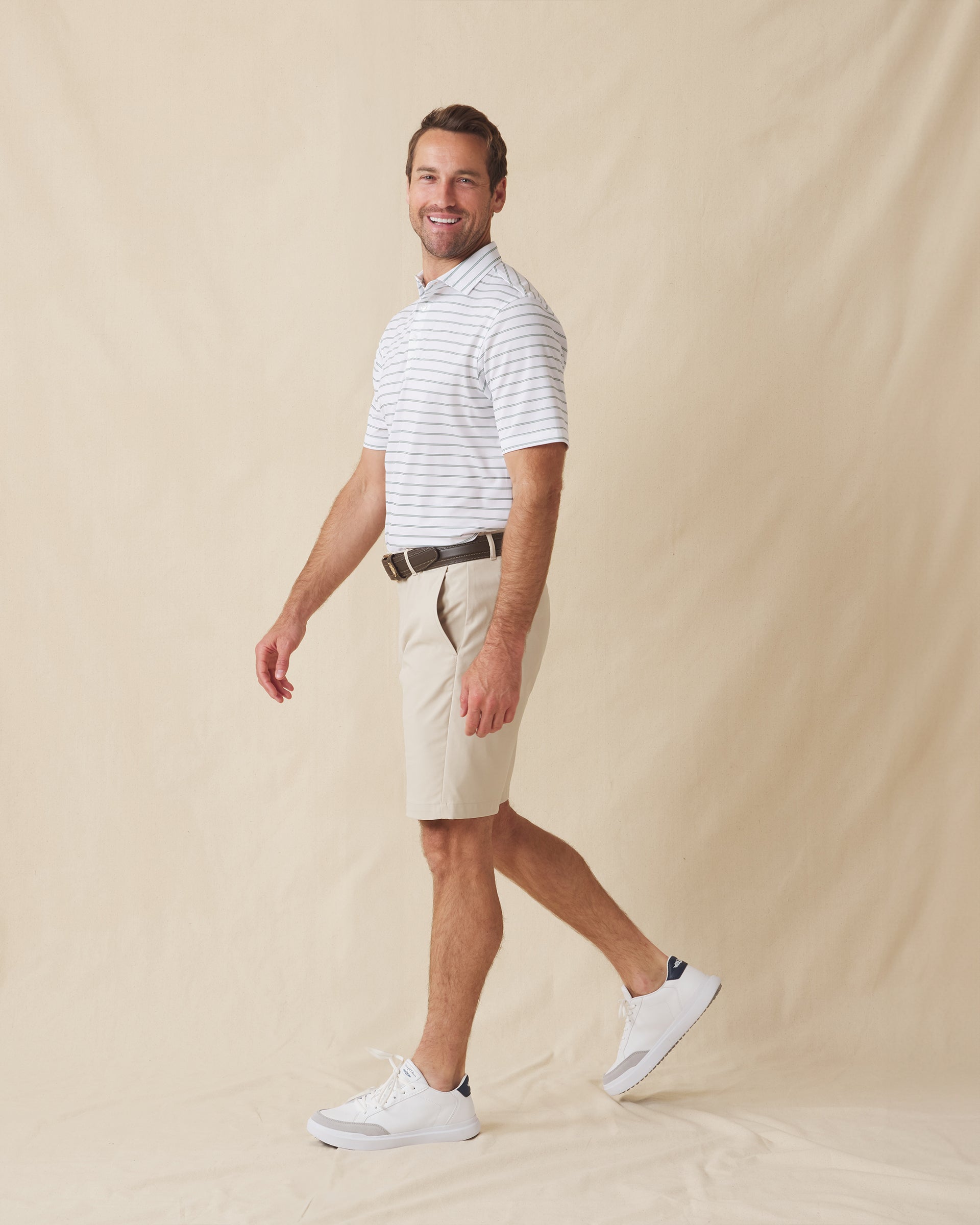 Men's Quintero Stripe Polo in Sage, full length model view featuring a white short sleeve polo with horizontal green and sage pencil stripes paired with khaki shorts and white shoes