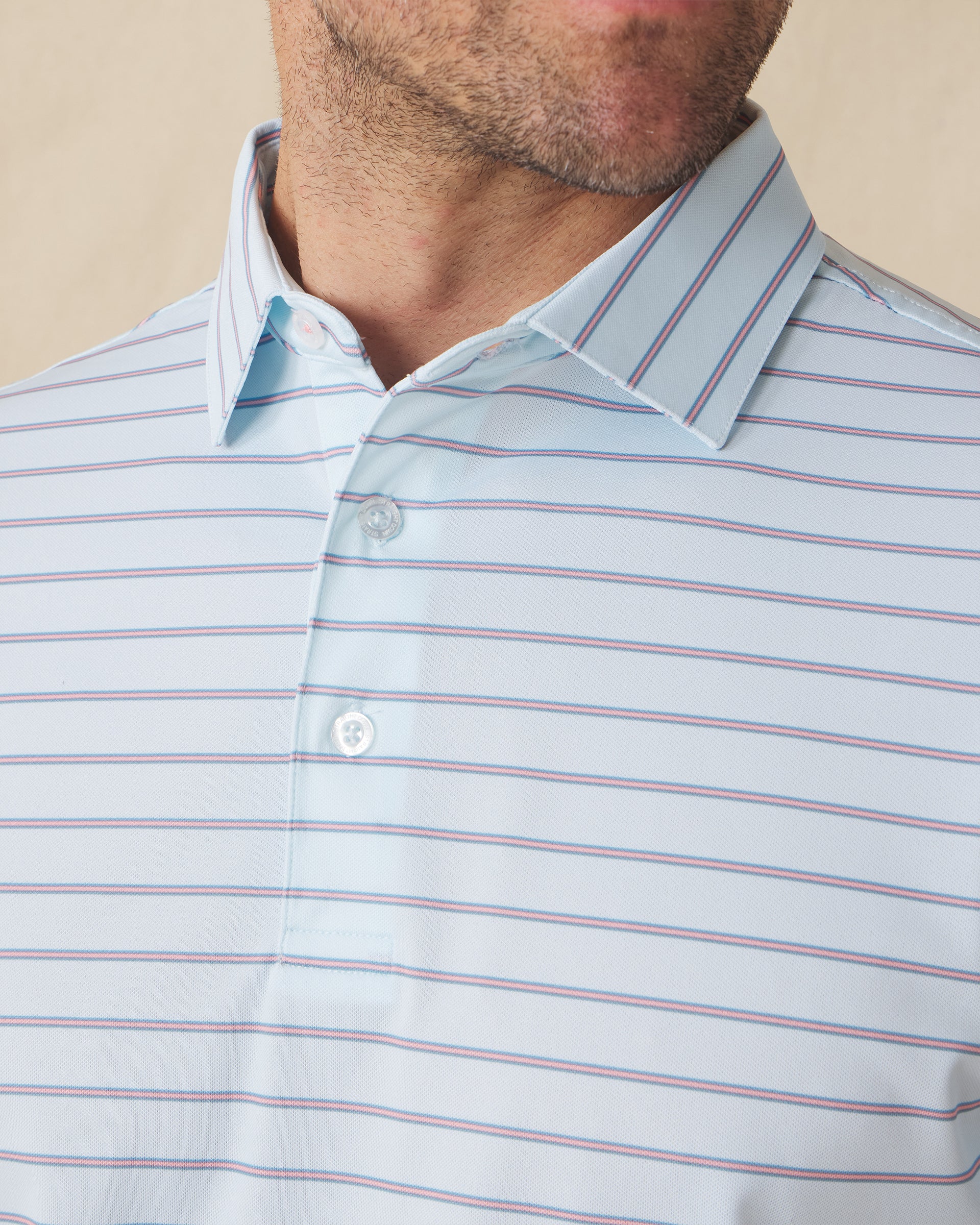 Men's Quintero Stripe Polo in Sea Spray, close-up model view featuring the collar and button placket detail of a light blue short sleeve polo with horizontal pink and steel blue pencil stripes