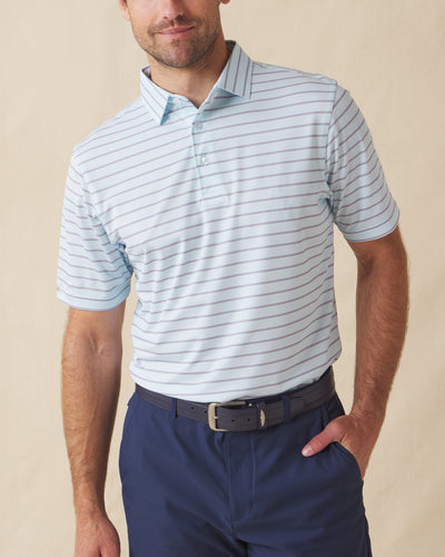 Men's Quintero Stripe Polo in Sea Spray, front model view featuring a light blue short sleeve polo with horizontal pink and steel blue pencil stripes paired with navy pants and a navy belt