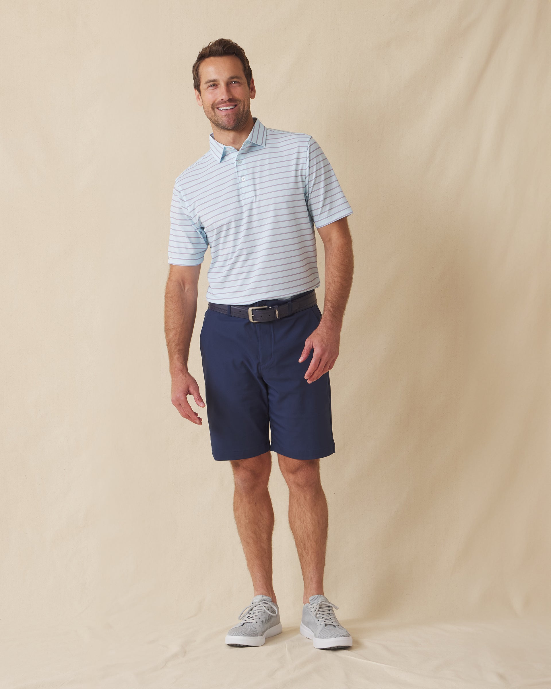 Men's Quintero Stripe Polo in Sea Spray, full length model view featuring a light blue short sleeve polo with horizontal pink and steel blue pencil stripes paired with navy shorts and gray shoes