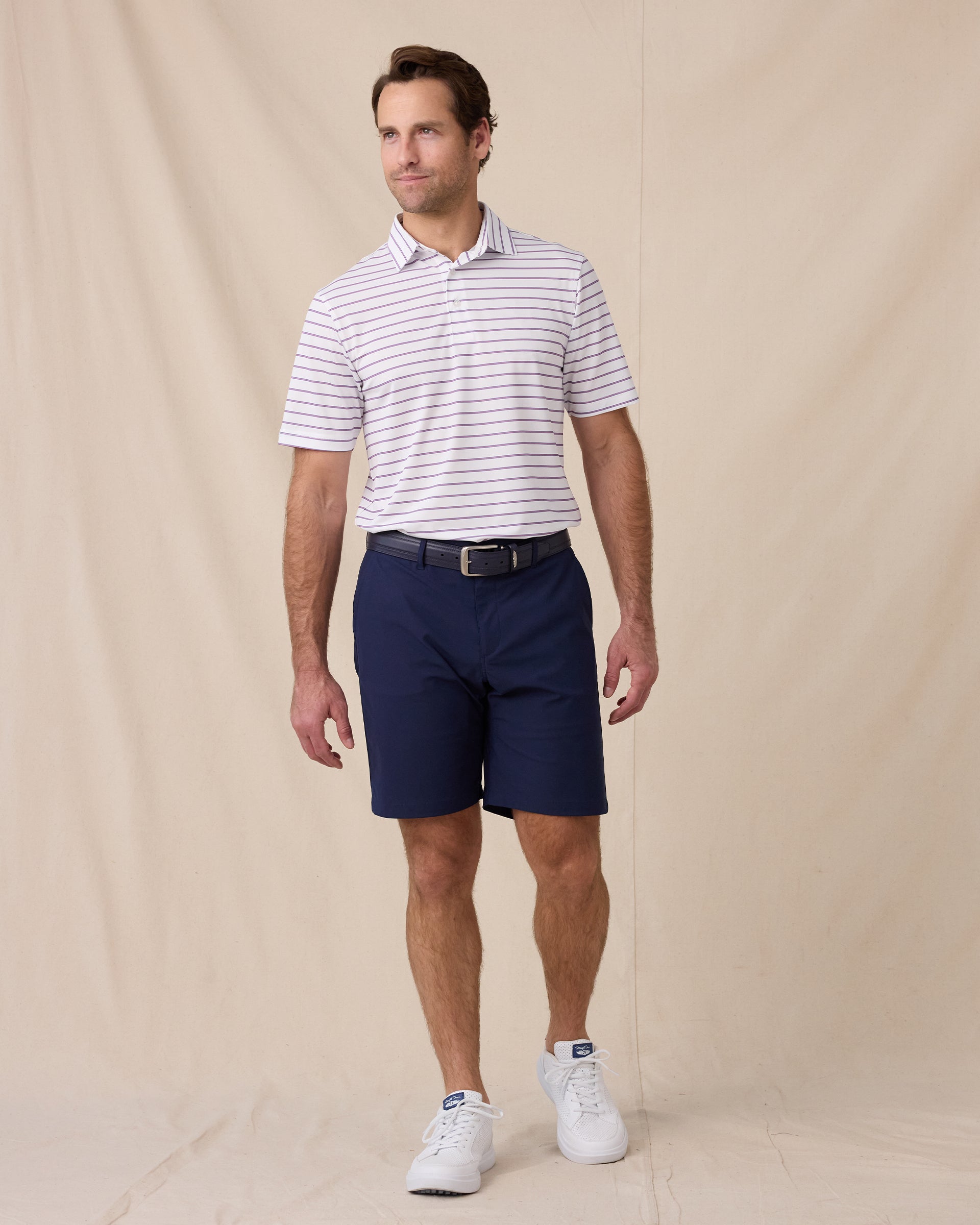Model wearing the Quintero Stripe Polo in Tidal paired with navy golf shorts, a navy belt, and white golf shoes