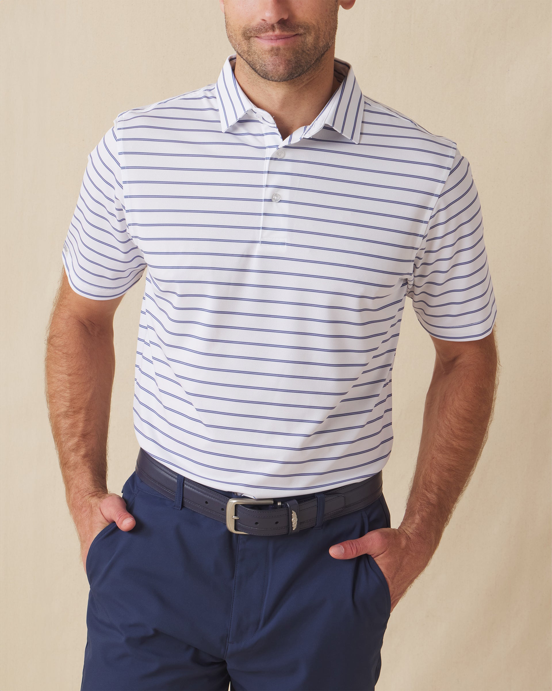 Men's Quintero Stripe Polo in Violet, front model view featuring a white short sleeve polo with horizontal blue and navy pencil stripes paired with navy pants and a navy belt