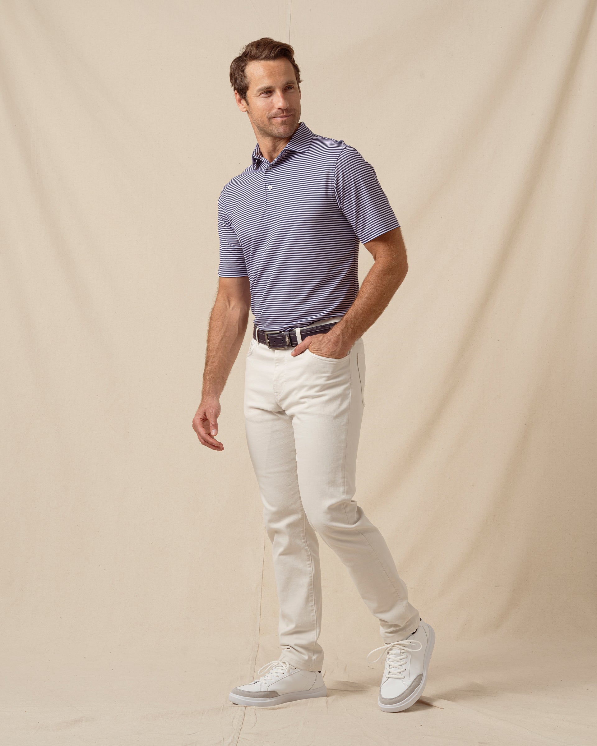Men’s indigo and lilac striped polo styled with light khaki pants, belt, and white sneakers