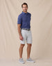 Men’s striped tidal blue polo styled with silver shorts, grey belt, and grey sneakers
