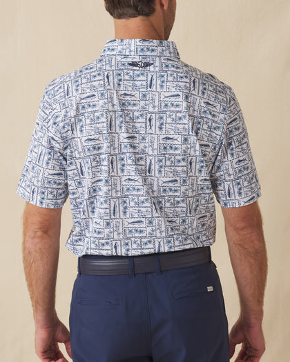 Men's Dorado Polo in Coastal, back view on model featuring a white base with a navy and blue tiled fish, floral, and bamboo stamp print, with Straight Down logo embroidered at upper back