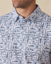 Men's Dorado Polo in Coastal, close-up front view on model highlighting the navy and blue tiled fish, floral, and bamboo stamp print on a white base
