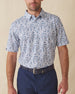 Men's Dorado Polo in Coastal, front view on model featuring a white base with a navy and blue tiled fish, floral, and bamboo stamp print, paired with navy pants and a dark leather belt