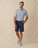 Men's Dorado Polo in Coastal, full length front view on model featuring a white base with a navy and blue tiled fish, floral, and bamboo stamp print, paired with navy shorts, a dark leather belt, and gray shoes