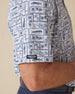 Men's Dorado Polo in Coastal, close-up sleeve view on model highlighting the Straight Down logo patch on the sleeve hem and the navy and blue tiled fish, floral, and bamboo stamp print