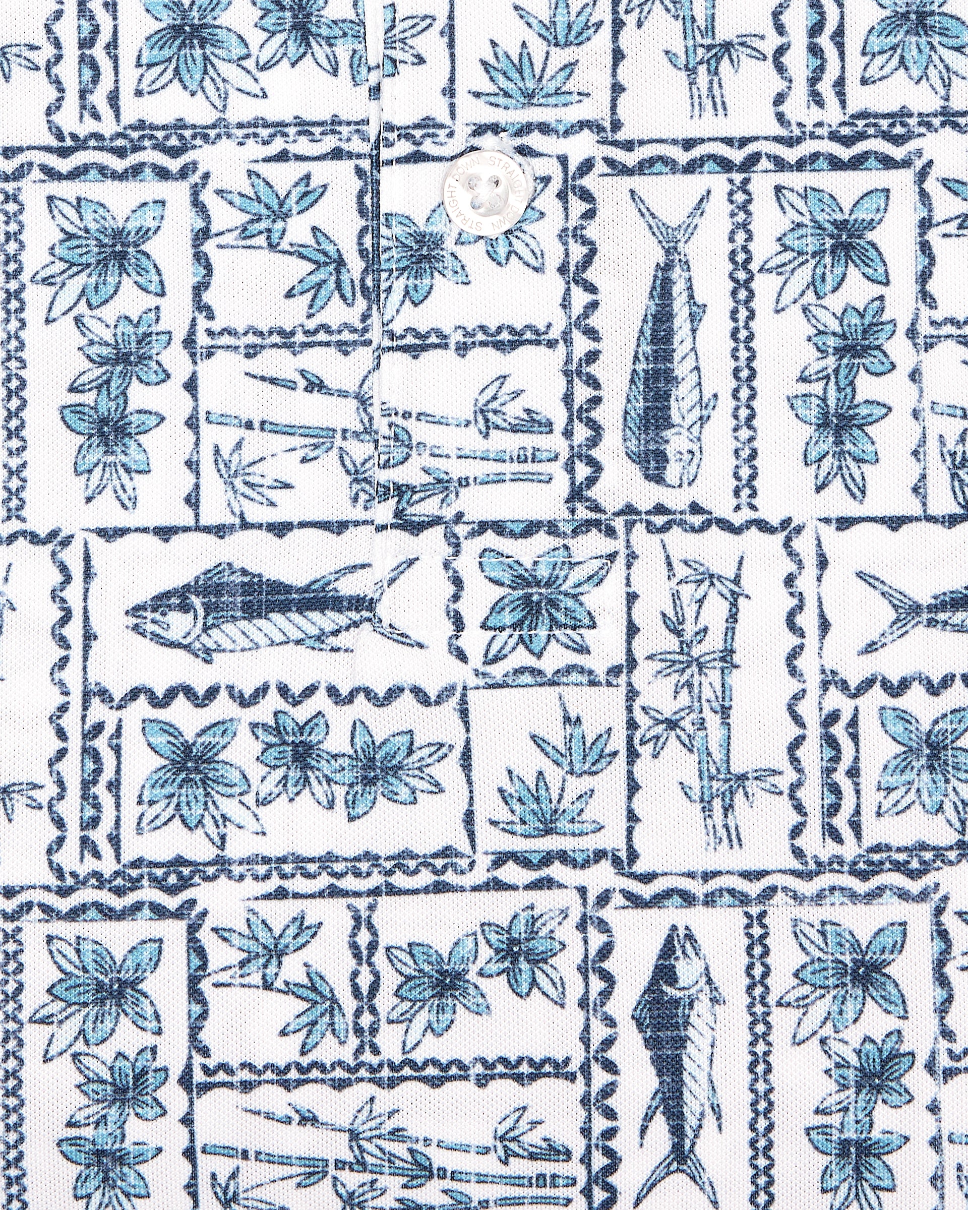 Men's Dorado Polo in Coastal, close-up flat lay fabric detail view highlighting the navy and blue tiled fish, floral, and bamboo stamp print on a white base