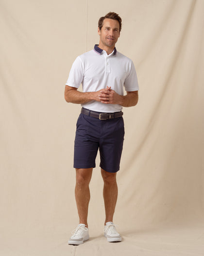 Men’s white polo with contrast navy and pink collar, paired with navy shorts and white sneakers