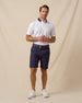 Men’s white polo with contrast navy and pink collar, paired with navy shorts and white sneakers