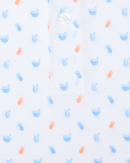 Men's Tropical Daze Polo in Carolina, close-up flat lay detail view featuring scattered pineapples and coconut drinks in sky blue and peach on a white ground with a branded button at the placket