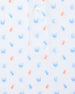 Men's Tropical Daze Polo in Carolina, close-up flat lay detail view featuring scattered pineapples and coconut drinks in sky blue and peach on a white ground with a branded button at the placket