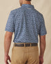 Men's Don Ho Polo in New Indigo, back view on model featuring a navy base with an all-over light blue floral print, with Straight Down logo embroidered at upper back, paired with khaki pants